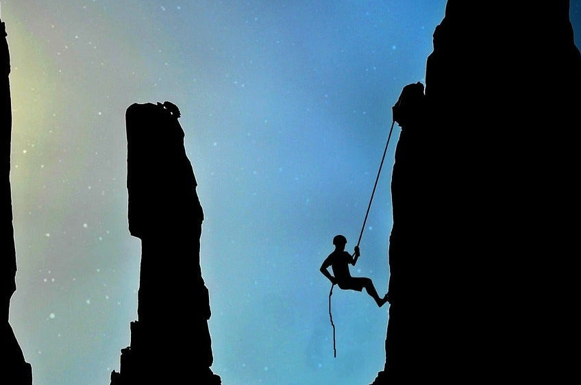 Silhouette of a climber ascending a rocky outcrop against a starry sky.